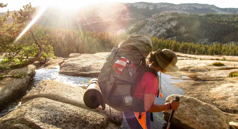 A person wearing a backpack crosses a stream in a mountain environment 